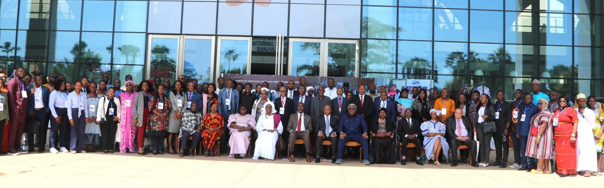 A wide photograph of NGO Forum delegates assembled outside the Sir Dawda Kairaba Jawara International Conference Centre in Banjul, October 2025